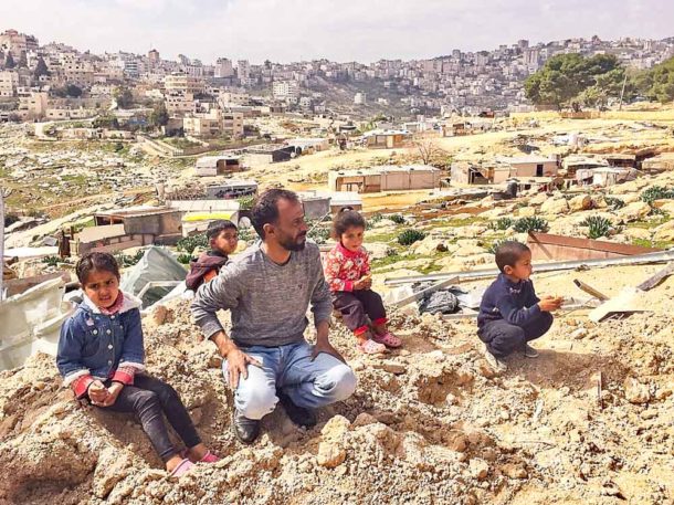A family sit at the site of their demolished home in Jabal Al Baba