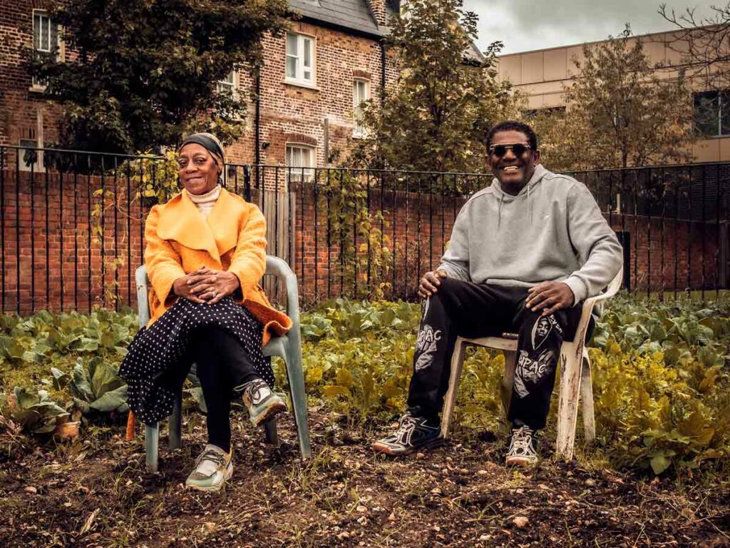 two gardeners sitting in front of vegetable patch