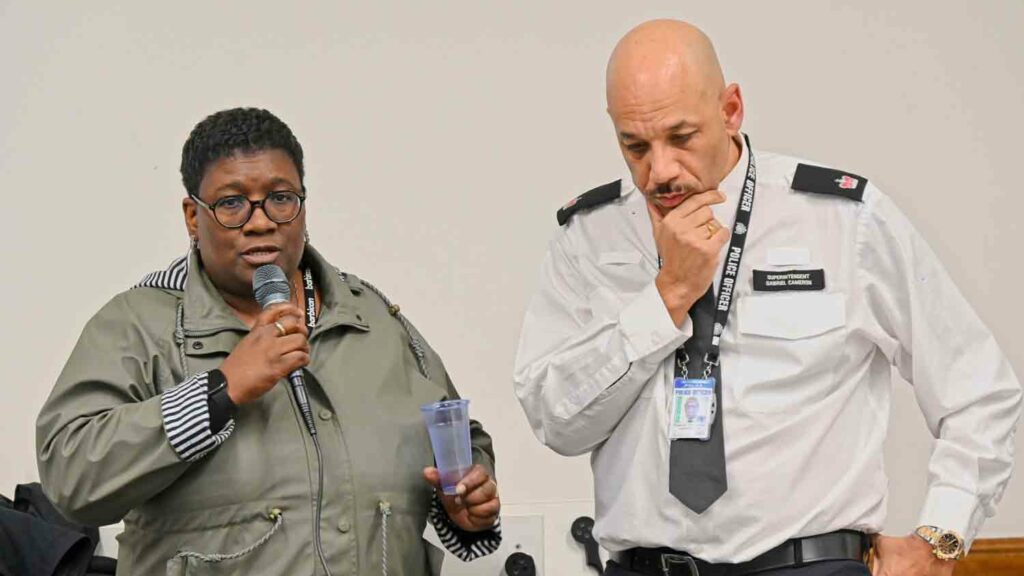 woman with mic at public meeting with police officer