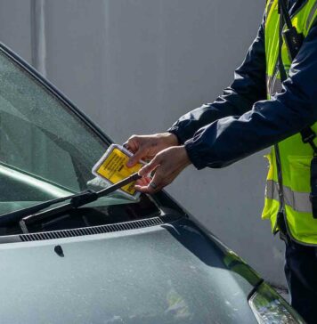 warden attaching parking ticket to windscreen