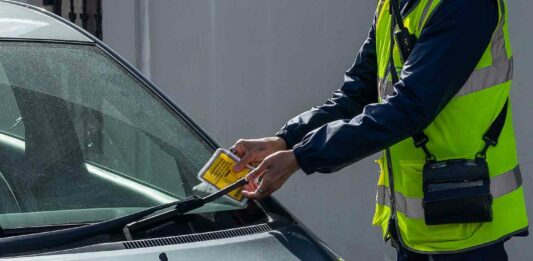 warden attaching parking ticket to windscreen