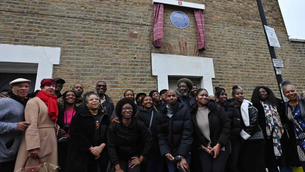 large group of people pose for photo beneath a memorial plaque